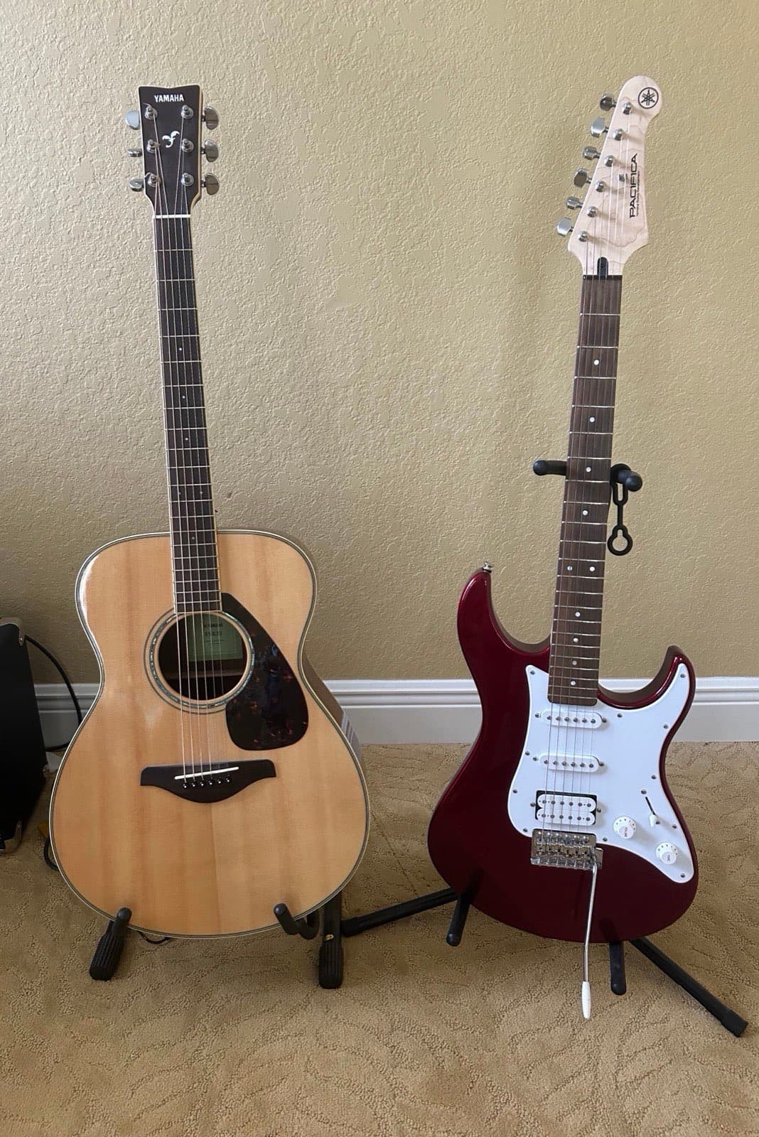 Two guitars on stands against a textured wall.